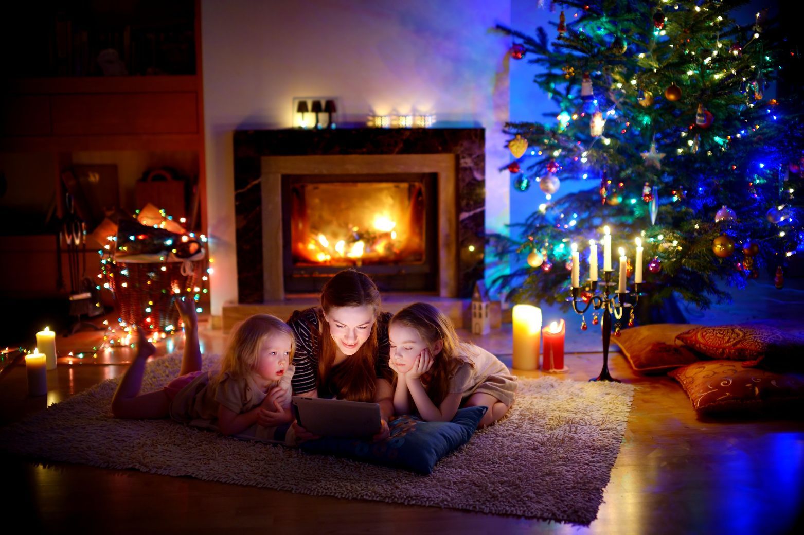 Mother and daughters using a tablet by a fireplace on Christmas